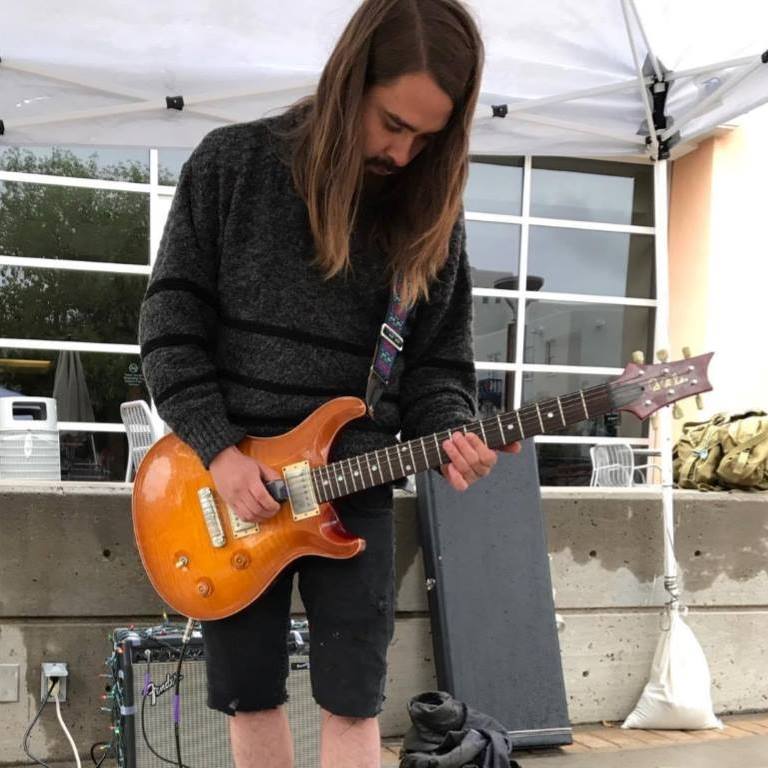 A photo of Batty Fang beneath a white canopy. They are holding an electric guitar.