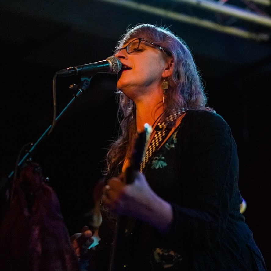 Photo of musician, "50 Foot Woman," singing at a microphone and playing a guitar.