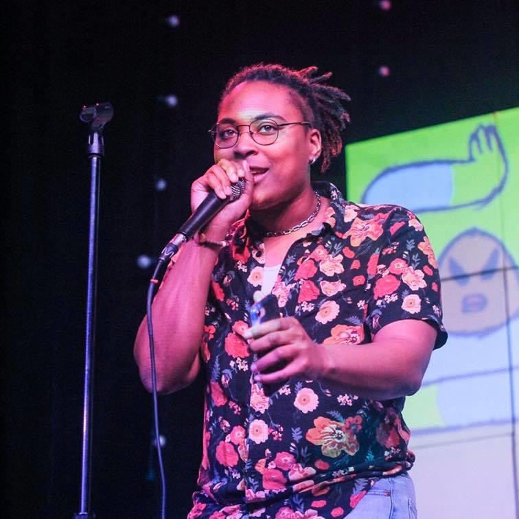 Photo of poet, KB, standing on a stage and talking into a microphone.